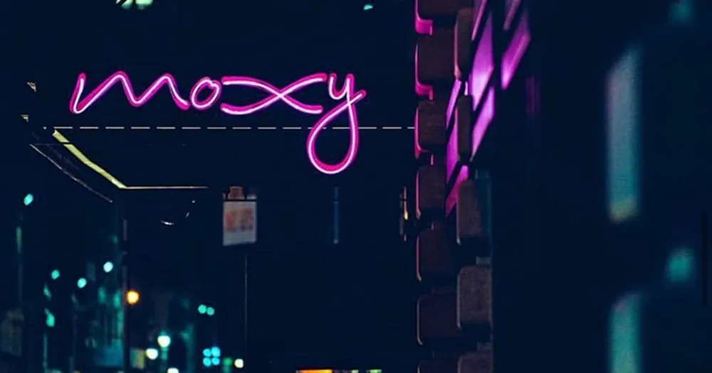 Pink Moxy neon sign on a dark building exterior