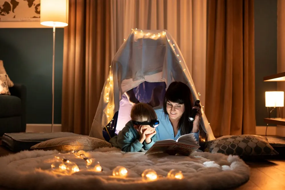 Bambini leggono sotto una tenda di coperte con lucine