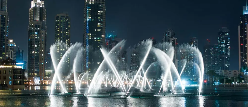 Jets de fontaine illuminés devant des immeubles de nuit