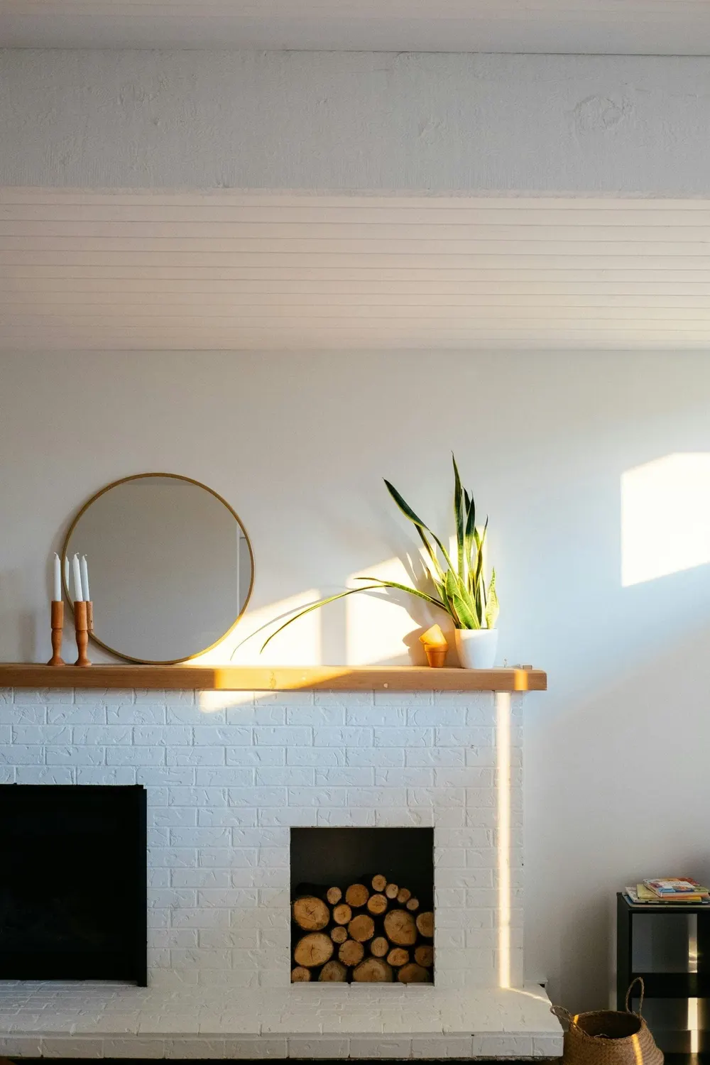 Espejo redondo y planta sobre una chimenea blanca