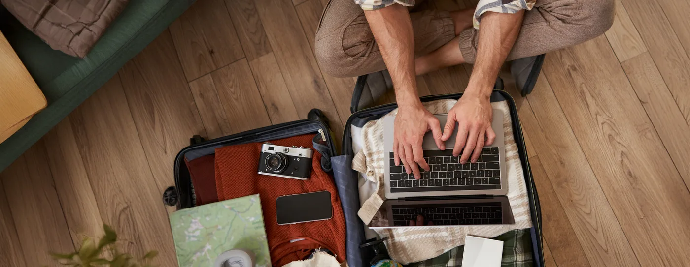 Reisender am Laptop neben einem offenen Koffer