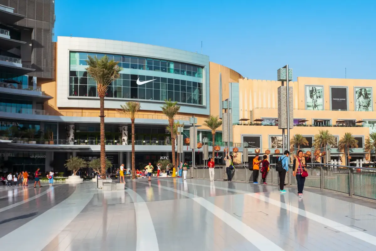 Open-air shopping plaza with palm trees and pedestrians