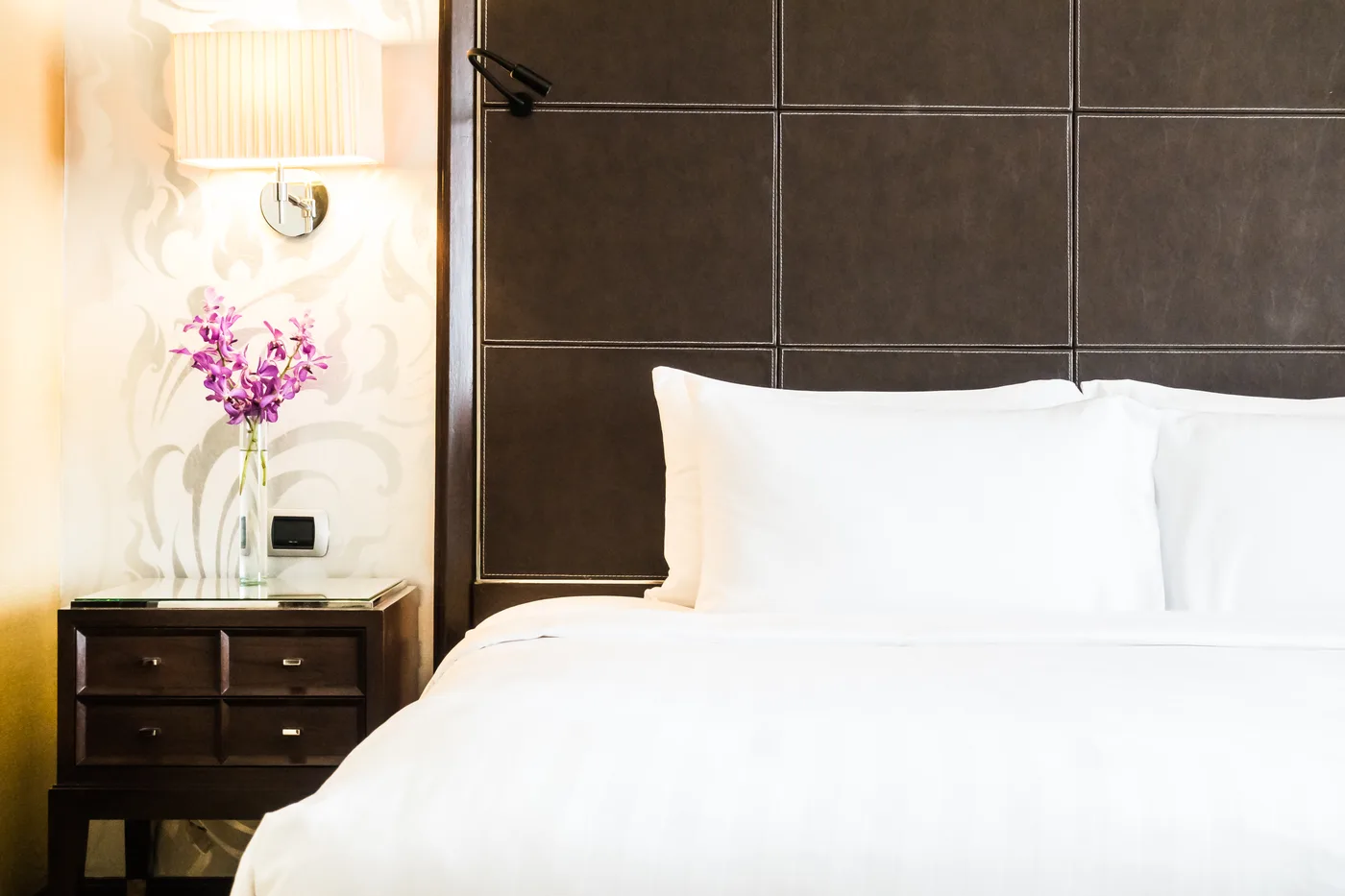 Letto bianco accanto a una lampada e fiori rosa