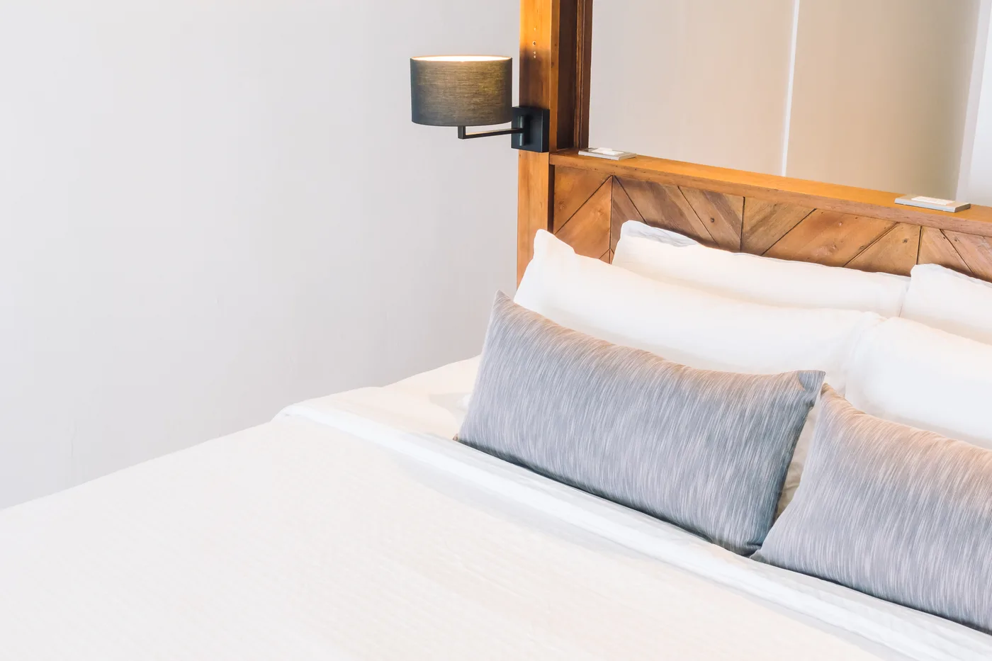 White bed with grey cushions and a wall-mounted lamp