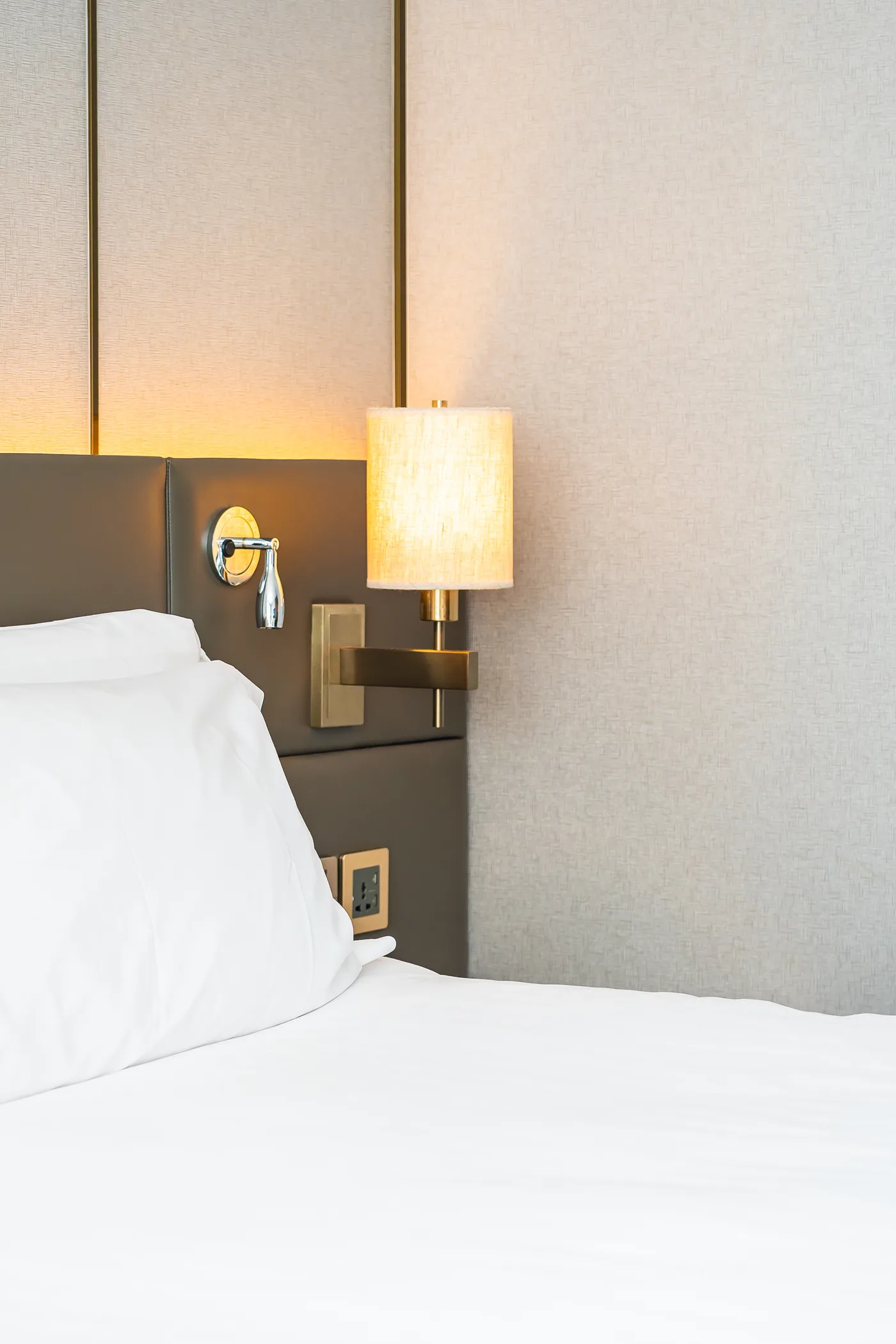 Ropa de cama blanca bajo una lámpara de pared