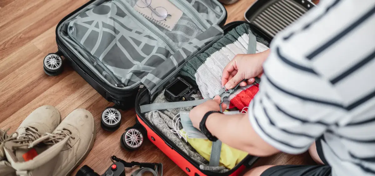 Traveller packing a red shirt into an open suitcase