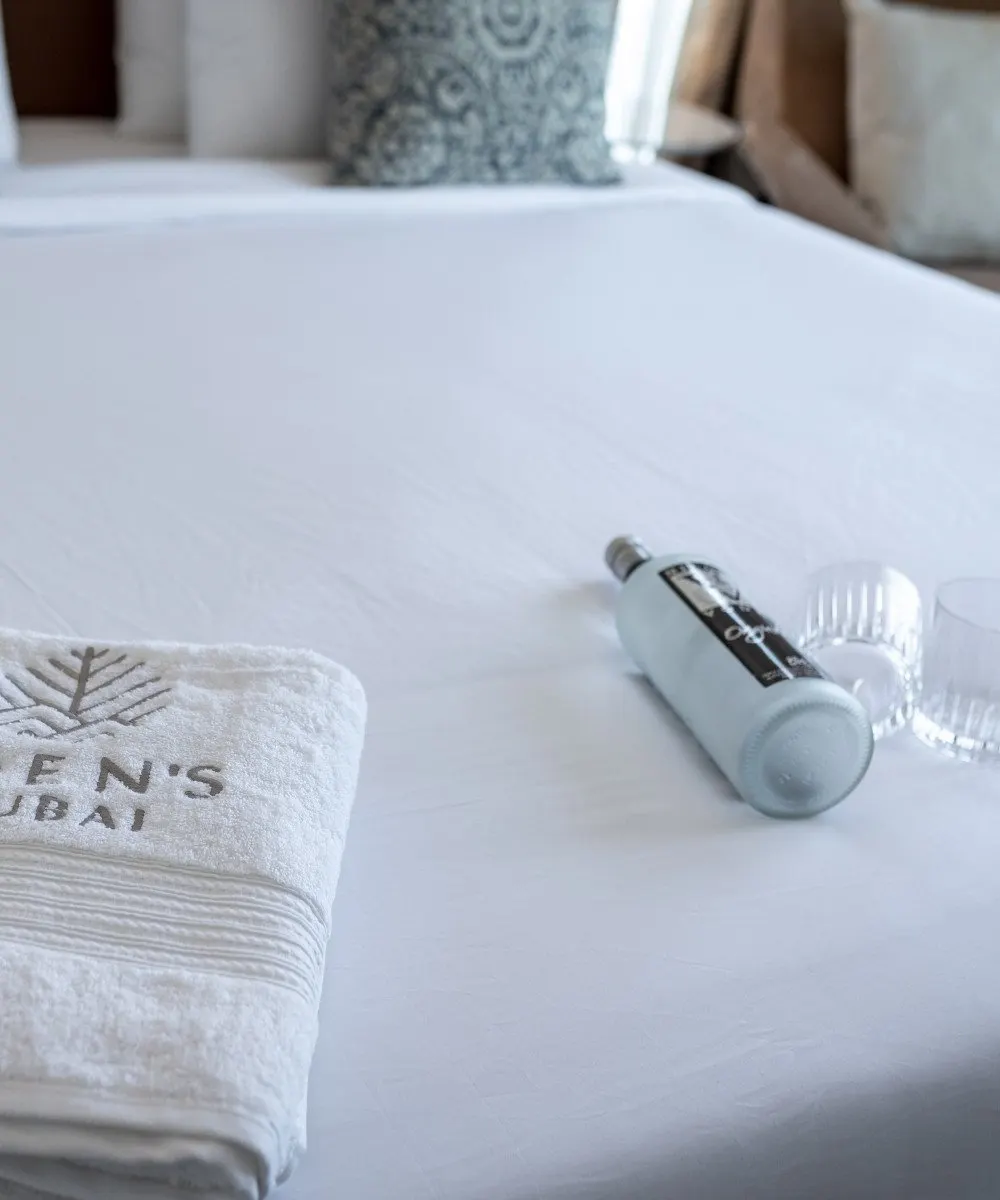 Toalla de huésped doblada y pequeños artículos de aseo sobre ropa de cama blanca